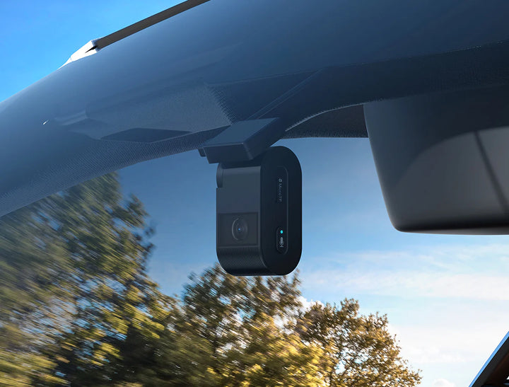 Car dashboard camera mounted on a car's windshield with trees and blue sky in the background.