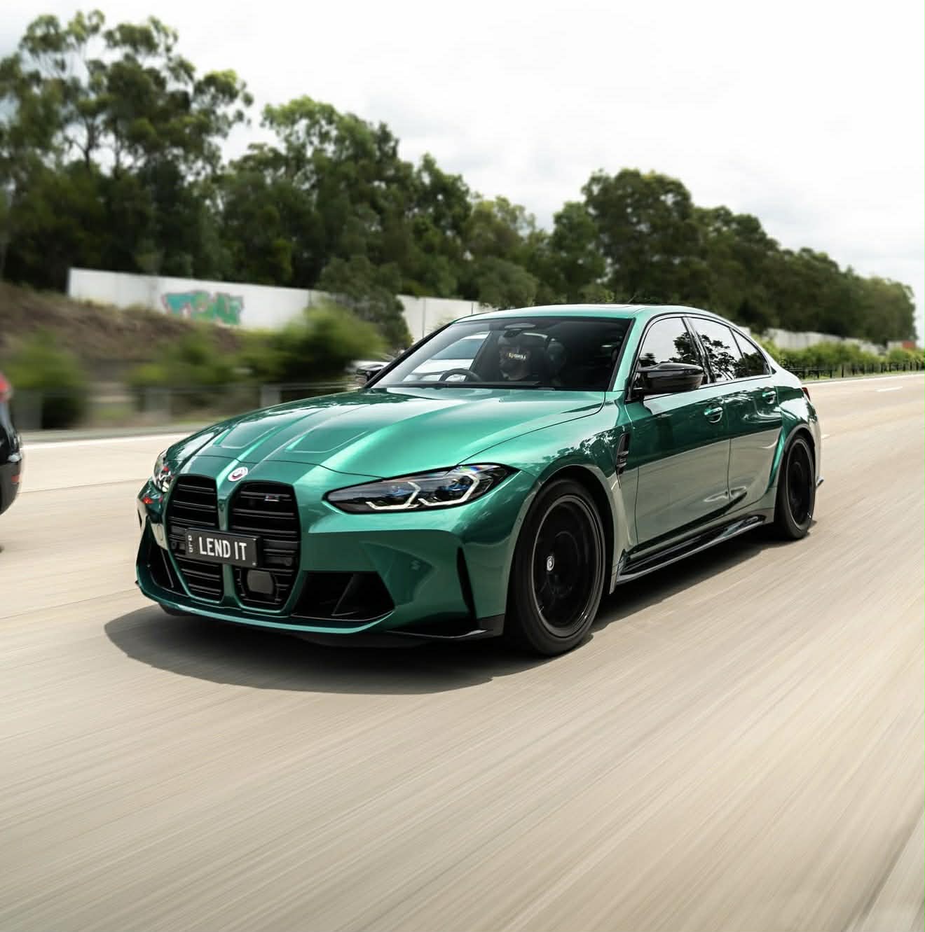 Green BMW car on a track with trees in the background